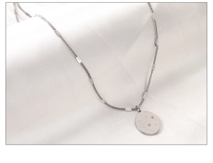 Detail of silver oval pendant with moon and star carvings on textured white fabric