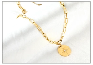 Detail view of golden paperclip chain necklace with a star-engraved oval pendant