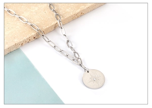 Detail of silver paperclip chain necklace with celestial star engraved oval pendant