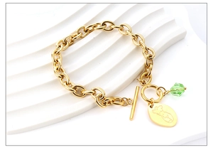 Detail von goldenem Gliederkettenarmband mit grünem Kristall und graviertem Anhänger