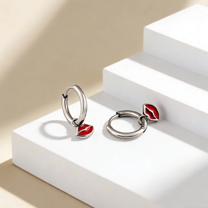 Close-up of silver earrings with red lip pendants on a white geometric display stand