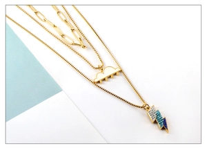 Detailed view of layered gold-plated necklaces with enamel cloud and crystal lightning pendants