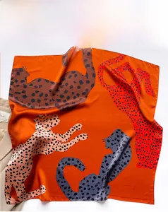 Detail of silk scarf showing orange fabric with artistic leopard prints and smooth texture