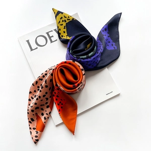 Detail shot of rolled leopard print silk scarves in navy and orange satin fabric