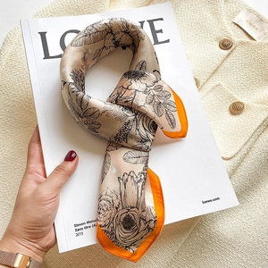 Detailed view of beige silk scarf with floral sketches and bright orange borders