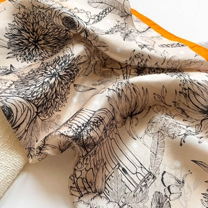 Close-up of silk scarf showing floral print details and vibrant orange hand-rolled edges