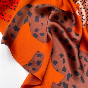 Macro view of leopard print silk scarf showing smooth texture and orange animal pattern