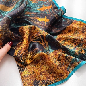Detail of silk scarf showing artistic gold crane print and smooth satin texture