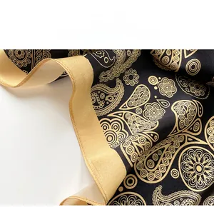 Detailed close-up of premium silk scarf featuring gold paisley print and reinforced hem