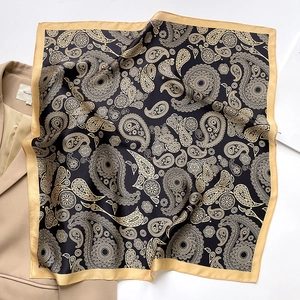 Close-up of black and gold Paisley silk scarf styled on a beige suit blazer
