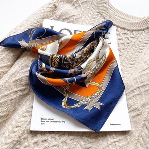 Navy and orange silk scarf with luxury chain print laid on a white book and beige knit