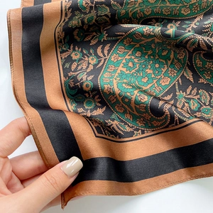 Detailed view of hand-held paisley silk scarf in vintage green and caramel brown tones
