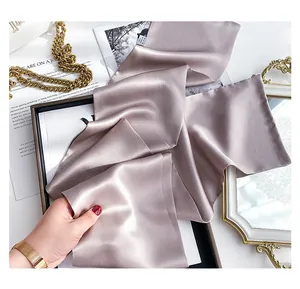 Detailed view of silk champagne gray satin skinny scarf on a luxury display tray