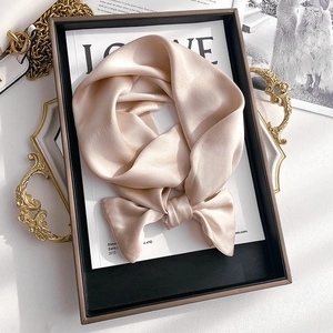 Close-up of champagne silk scarf with soft satin luster tied in a bow on a magazine