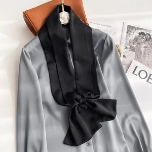 Detail of grey silk satin shirt featuring a large black bow tie and glossy finish texture