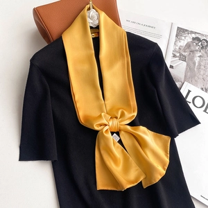 Close-up of bright yellow silk scarf tied in a bow on a black knitted top detail