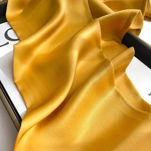 Macro shot of elegant golden silk scarf fabric showing smooth satin texture and drape