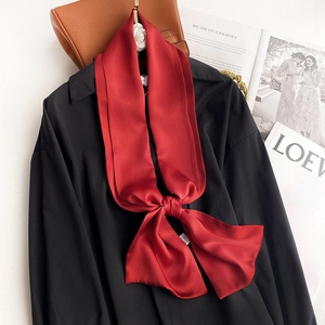 Detail of red silk scarf tied in a bow against black shirt and high-end accessories