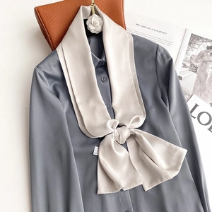 Close-up of a champagne silk scarf tied in a bow on a lustrous blue professional blouse
