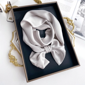 Close-up of a silver silk scarf with pearl luster folded in a bow on a black tray