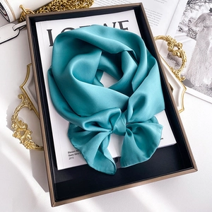 Detail of luxury solid cyan silk scarf tied in a bow on a stylish vintage tray display
