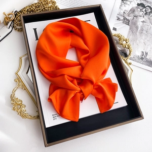 Macro shot of vibrant orange silk scarf textured fabric layered on fashion books
