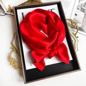 Detailed view of luxury red silk scarf tied in a bow on a tray with artistic magazines