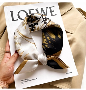 Detailed view of a knotted silk square scarf with gold and black leaf print on a trench coat