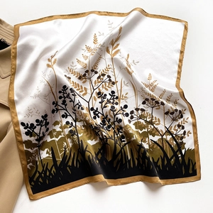 Close-up of silk square scarf with floral silhouette print and golden hem on a trench coat