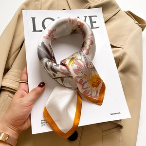 Detail of silk scarf with floral print and yellow border on a camel trench coat