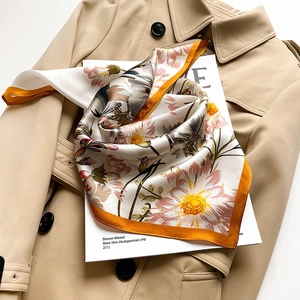 Silk floral square scarf with daisy print and orange border styled on a khaki trench coat