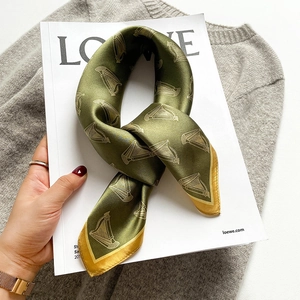 Dark green silk scarf with golden harp patterns and yellow borders on a magazine