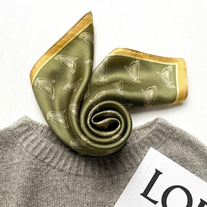 Elegant olive green silk scarf with gold harp patterns on a grey knit sweater