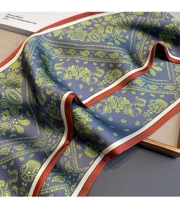 Macro detail of silk-like blue paisley scarf with red border on a wooden tray