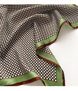 Détail d'un foulard en soie avec motif géométrique vert et marron et bords roulés