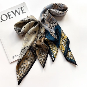 Detailed close-up of a printed silk square scarf with golden chain and palm patterns