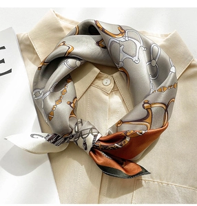 Close-up of silk square scarf with horse chain print styled on a beige shirt collar