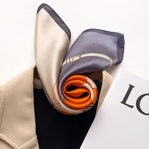 Silk neck scarf with orange and grey horse bit pattern styled on a beige blazer suit