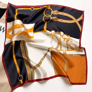 Silk scarf with equestrian bridle print in navy and orange draped over magazine