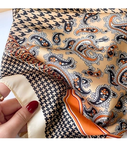 Close-up of silk-textured square scarf with golden paisley and houndstooth patterns