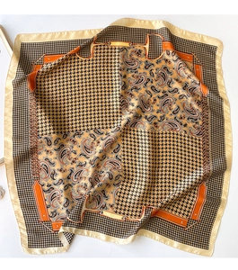 Detail of silk-like scarf featuring orange houndstooth, paisley, and chain patterns