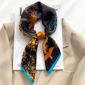 Sciarpa in seta con motivi astratti arancio e blu annodata su un blazer beige elegante