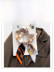 Détail d'un carré de soie avec mors et chaîne posé sur un blazer marron à chevrons