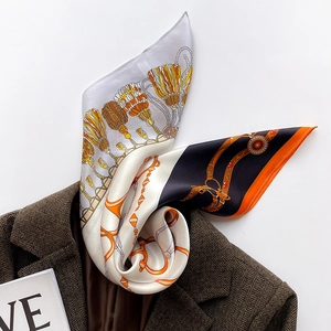 Carré de soie luxueux avec imprimé chaînes et glands posé sur un blazer marron chic