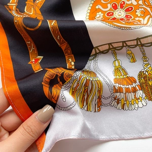 Détail macro du carré en soie avec motifs équestres et finition satinée orange