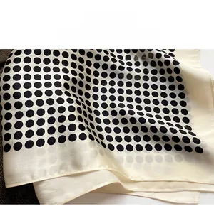 Détail macro de l'ourlet de précision sur un foulard en soie beige à pois noirs