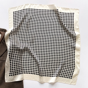 Gros plan d'un foulard en soie à pois blanc sur un blazer en laine marron à chevrons