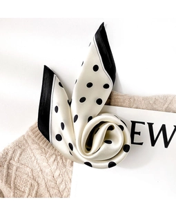 Detailed view of silk polka dot scarf with black border on a cream sweater