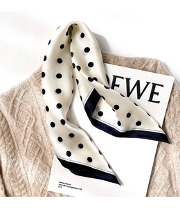 Detail shot of a polka dot silk scarf on a beige sweater with an artistic card background