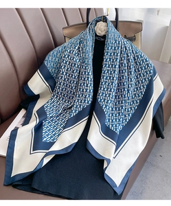 Close-up of geometric chain print square scarf draped elegantly on a leather sofa